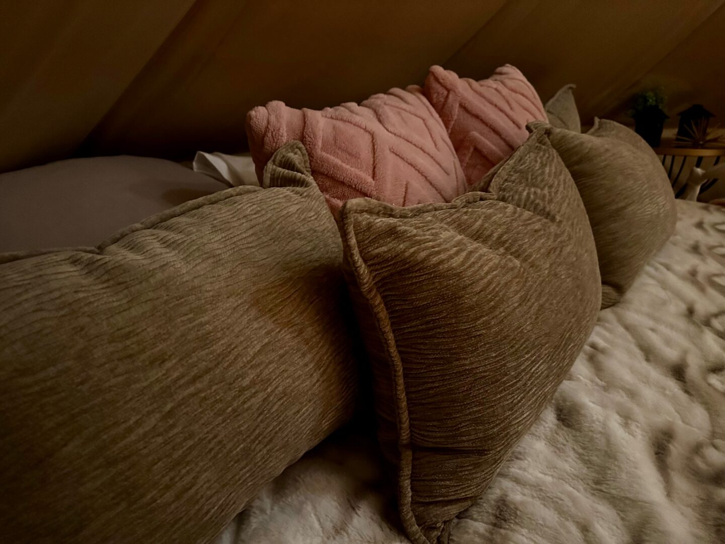 Detalle cercano de almohadas rosa y salvia en la cama de una tienda campana.